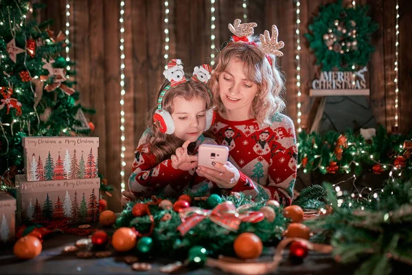 Мати і дочка дивляться телефон поруч з ялинкою і покупки онлайн — стокове фото