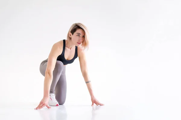 Gezonde jonge vrouw bereidt zich voor op een run. Fit vrouwelijke atleet klaar voor een voorjaar over witte achtergrond met kopieerruimte — Stockfoto