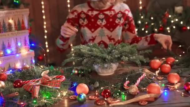 ผู้หญิงที่แต่งตัวในวันคริสต์มาสออกแบบเสื้อกันหนาวทํามือคริสต์มาส wreath บนโต๊ะสําหรับวันหยุด การตกแต่งคริสต์มาสและการประกอบ — วีดีโอสต็อก