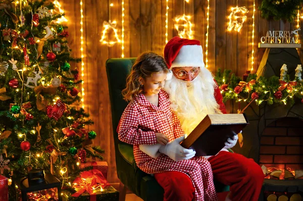 Санта Клаус відкрив і прочитав магічну книжку з маленькою милою дівчиною в піжамі. — стокове фото