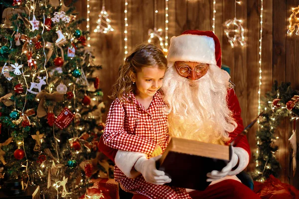 Père Noël ouvert et lire livre magique avec petite fille mignonne étonnée en pyjama — Photo