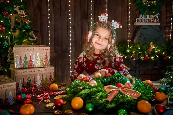 Petite fille décorant une couronne de conifères près du sapin de Noël à l'intérieur décoratif. Noël et Nouvel An photo — Photo