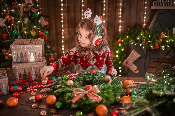 Petite fille décorant une couronne de conifères près du sapin de Noël à l'intérieur décoratif. Noël et Nouvel An photo — Photo