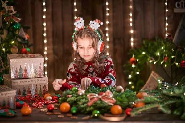 Petite fille décorant une couronne de conifères près du sapin de Noël à l'intérieur décoratif. Noël et Nouvel An photo — Photo