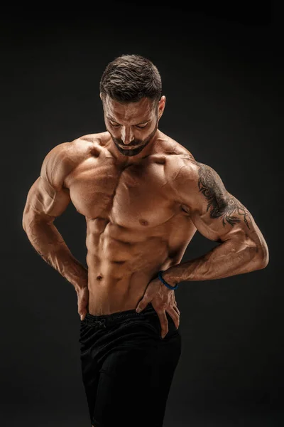 Bodybuilder poseren. Fitness gespierde man op donkere achtergrond. — Stockfoto