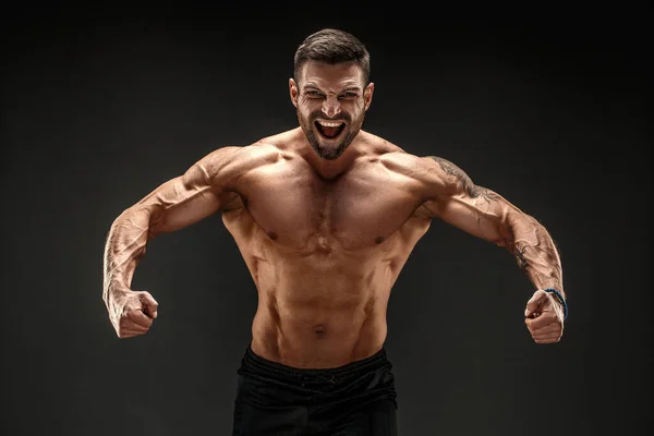 Bodybuilder posing. Fitness muscled man on dark background. Roaring for motivation. — Stock Photo, Image