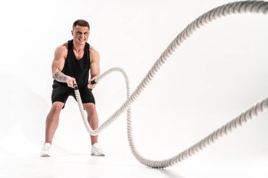 Çekici kaslı adam ağır iplerle çalışıyor. Beyaz arka planda izole edilmiş spor giysili yakışıklı bir adamın fotoğrafı.