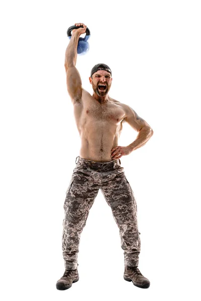 Atleta muscolare uomo bodybuilder in pantaloni mimetici con un allenamento nudo del busto con kettlebell su sfondo bianco. — Foto Stock