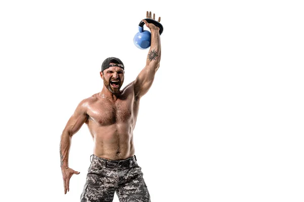 Atleta muscolare uomo bodybuilder in pantaloni mimetici con un allenamento nudo del busto con kettlebell su sfondo bianco. — Foto Stock