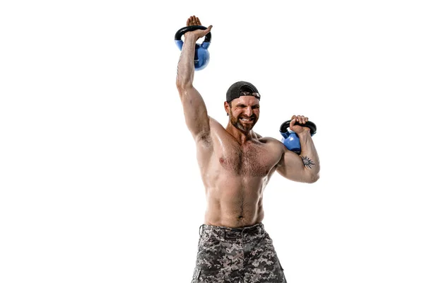 Muskulös idrottare bodybuilder man i camouflage byxor med en naken bål träning med kettlebell på en vit bakgrund. — Stockfoto