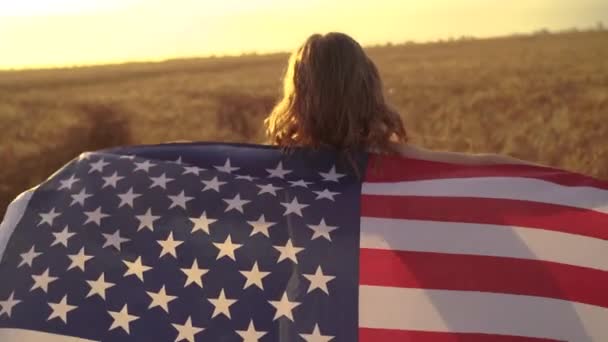 Chica en vestido blanco con una bandera americana mientras corre en un hermoso campo de trigo — Vídeos de Stock