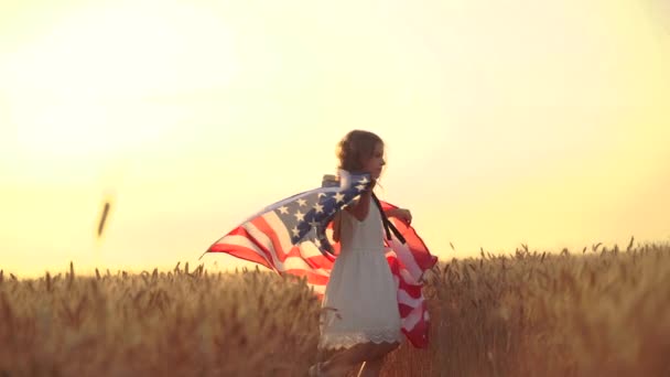 Chica en vestido blanco con una bandera americana mientras corre en un hermoso campo de trigo — Vídeos de Stock