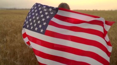 Gün batımında güzel bir buğday tarlasında koşarken küçük kız Amerikan bayrağı takıyor.