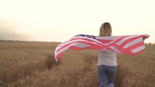 Donna che corre e salta spensierata con le braccia aperte sul campo di grano Tenendo bandiera USA — Video Stock