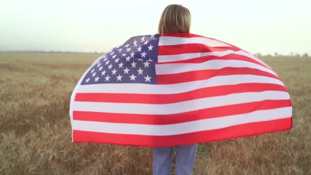 Žena běží a skákání bezstarostné s otevřenou náručí přes pšeničné pole Holding USA vlajka — Stock video