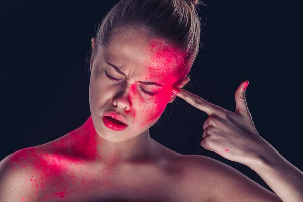 Mujer en maquillaje fantástico, polvo rojo, piel oscura sobre fondo oscuro, sosteniendo el dedo en la sien, simulando un disparo —  Fotos de Stock