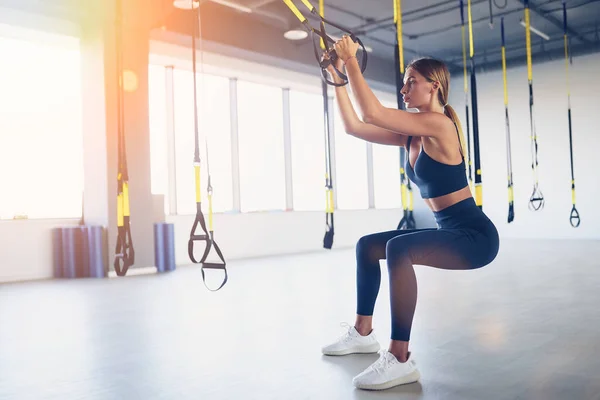 Beautiful young woman training with suspension trainer sling or suspension straps in gym. Upper body exercise concept on TRX