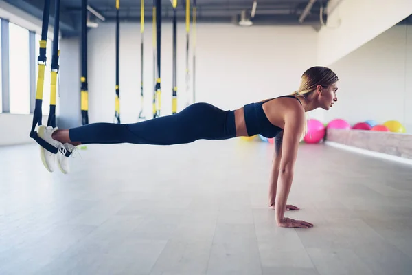 Hermosa joven entrenando con tirantes de suspensión o correas de suspensión en el gimnasio. Concepto de ejercicio corporal superior en TRX —  Fotos de Stock