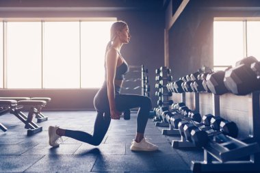 Güzel bir kız spor salonunda dambıllarla hareket ediyor.