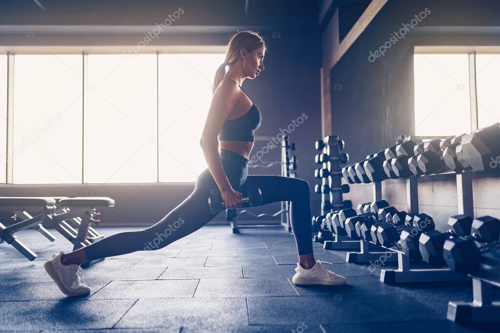 Beautiful girl doing lunges exercise with dumbbells in gym