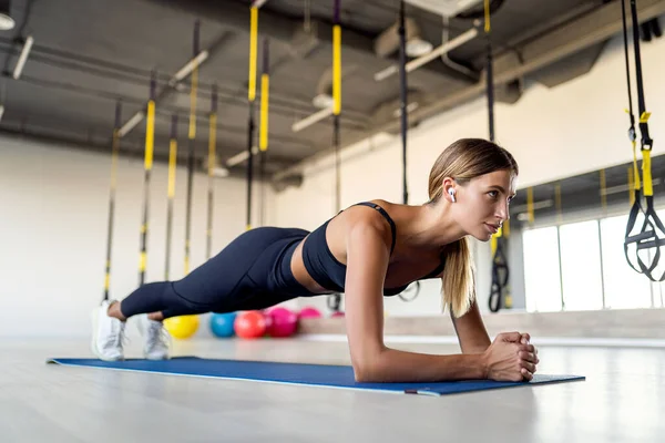 Volle Länge der jungen schönen Frau in Sportbekleidung, die Planke macht und ihre Kernmuskeln im Fitnessstudio trainiert — Stockfoto
