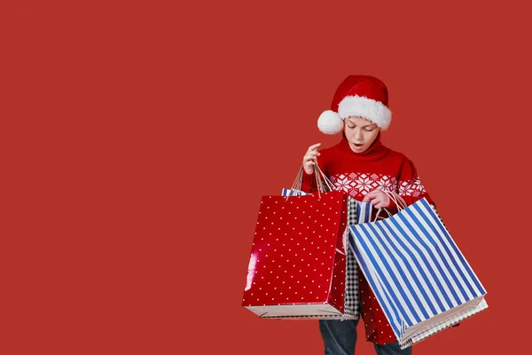 Lindo chico en suéter rojo sosteniendo bolsas de compras con regalos de Navidad — Foto de Stock