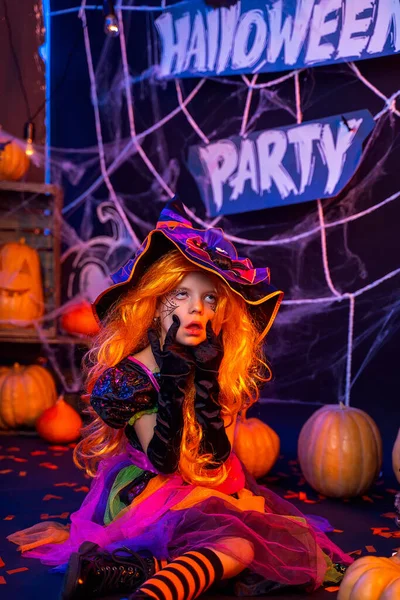 Malá krásná dívka v kostýmu čarodějnice slaví Happy Halloween party v interiéru s dýněmi — Stock fotografie
