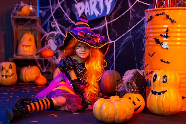 Pequena menina bonita em um traje de bruxa celebra festa de Halloween feliz no interior com abóboras — Fotografia de Stock