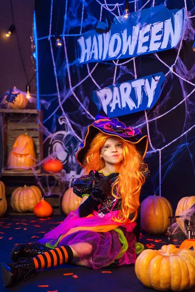 Malá krásná dívka v kostýmu čarodějnice slaví Happy Halloween party v interiéru s dýněmi — Stock fotografie