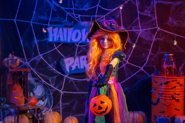 Pequeña chica hermosa en un disfraz de bruja celebra feliz fiesta de Halloween en el interior con calabazas — Foto de Stock