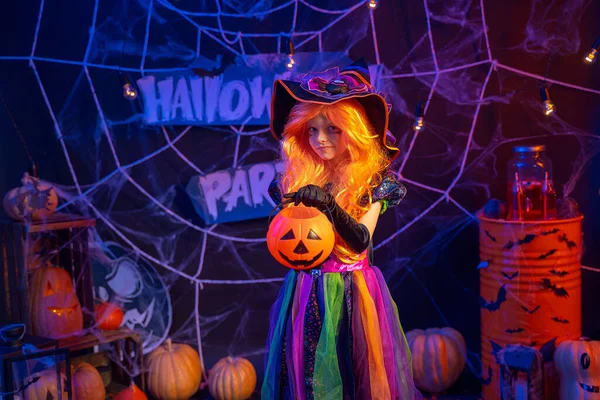 Pequeña chica hermosa en un disfraz de bruja celebra feliz fiesta de Halloween en el interior con calabazas — Foto de Stock