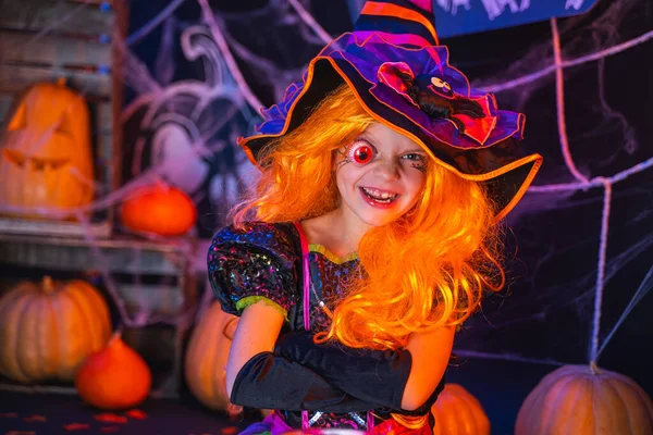 Маленькая красивая девочка в костюме ведьмы празднует Хэллоуин в интерьере с тыквами — стоковое фото