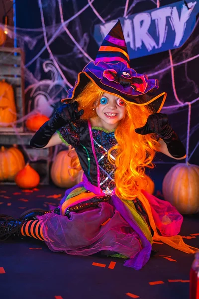 Pequena menina bonita em um traje de bruxa celebra festa de Halloween feliz no interior com abóboras — Fotografia de Stock