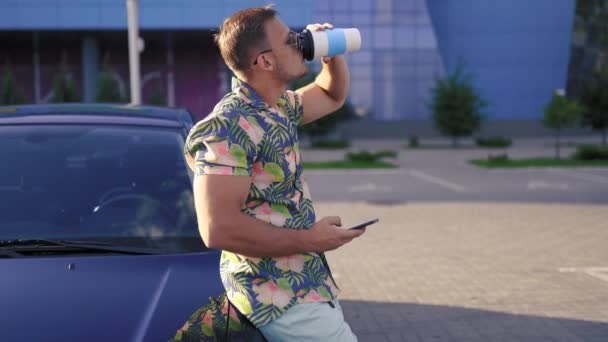 Jonge knappe man met drank wacht op vriend in de buurt van de stad parkeren — Stockvideo