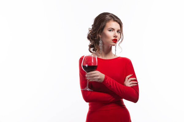 Woman with makeup, hairstyle waering red dress posing with glass of vine over white background, isolate