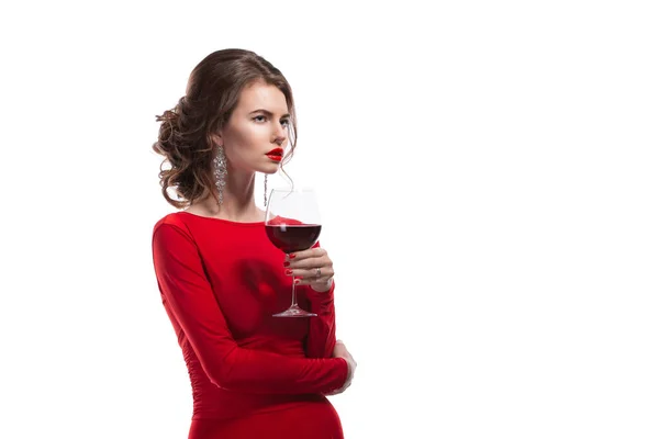 Woman with makeup, hairstyle waering red dress posing with glass of vine over white background, isolate — Stock Photo, Image