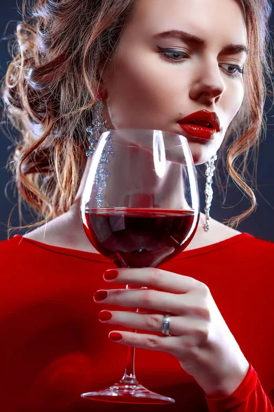 Kobieta z makijażem, fryzura obstawianie czerwona sukienka pozowanie ze szklanką wina na ciemnym tle, izolat — Zdjęcie stockowe