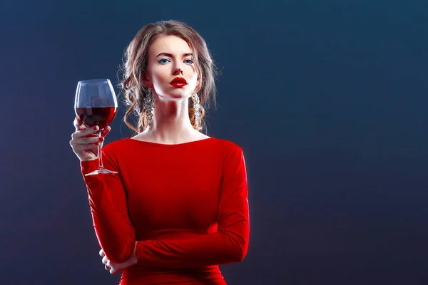 Woman with makeup, hairstyle waering red dress posing with glass of vine over dark background, isolate — Stock Photo, Image