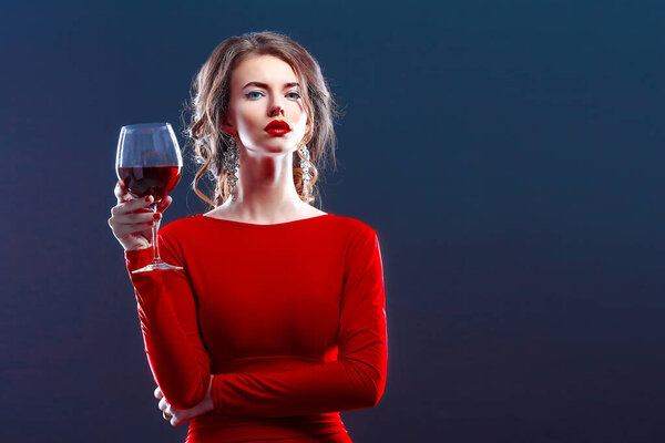 Woman with makeup, hairstyle waering red dress posing with glass of vine over dark background, isolate