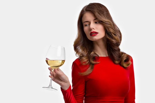 Woman with makeup, hairstyle waering red dress posing with glass of vine over white background, isolate — Stock Photo, Image