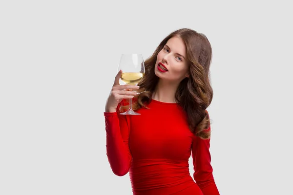 Woman with makeup, hairstyle waering red dress posing with glass of vine over white background, isolate — Stock Photo, Image