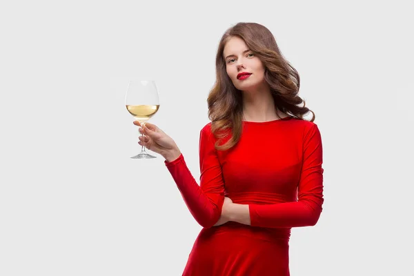Woman with makeup, hairstyle waering red dress posing with glass of vine over white background, isolate — Stock Photo, Image