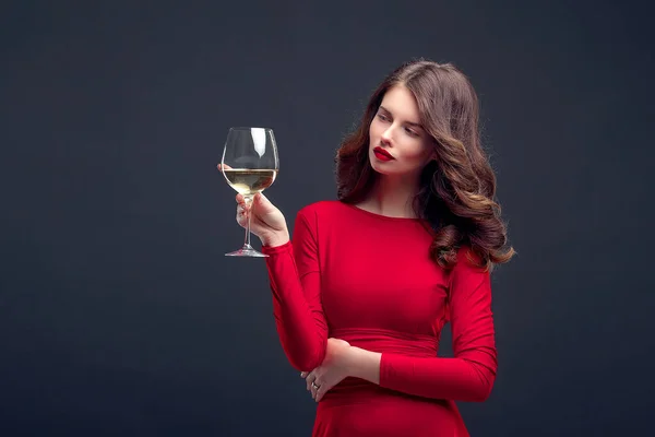 Mujer con maquillaje brillante, peinado con vestido rojo posando con vidrio de vid sobre fondo oscuro, aislar — Foto de Stock