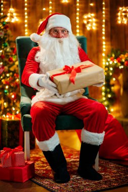 Mutlu Noel Baba 'nın dışarıda çocuklar için hediye kutusu tutarken çekilmiş bir fotoğrafı.