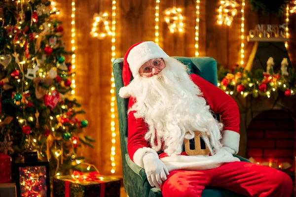 Der Weihnachtsmann sitzt am Weihnachtsbaum, am Kamin und blickt in die Kamera. Innenräume — Stockfoto