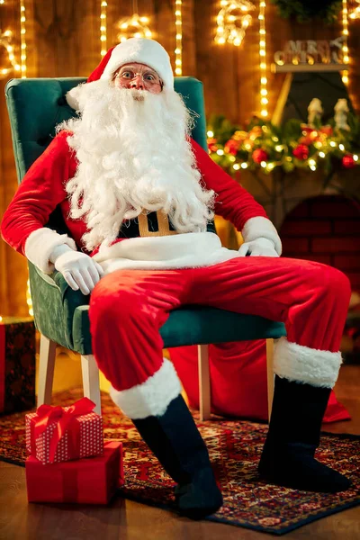 Der Weihnachtsmann sitzt am Weihnachtsbaum, am Kamin und blickt in die Kamera. Innenräume — Stockfoto