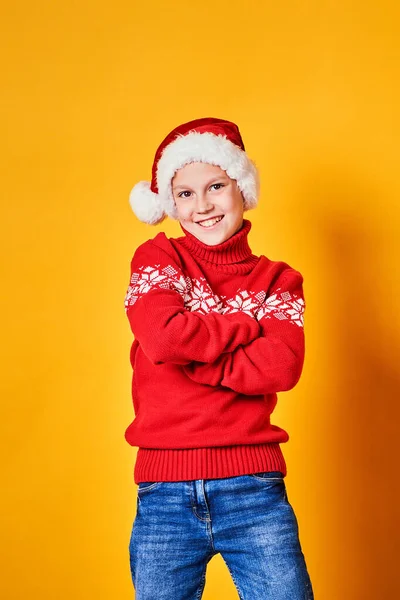 Niño en sombrero de Santa y suéter rojo posando el día de Navidad sobre fondo amarillo —  Fotos de Stock