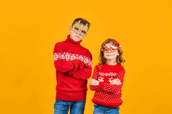 Enfants en pull de Noël rouge chaud et lunettes décorées regardant la caméra sur fond jaune — Photo