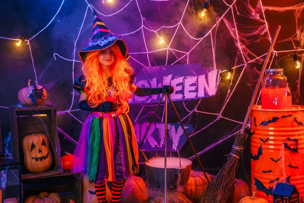 Malá krásná dívka v kostýmu čarodějnice slaví Happy Halloween party v interiéru s dýněmi — Stock fotografie