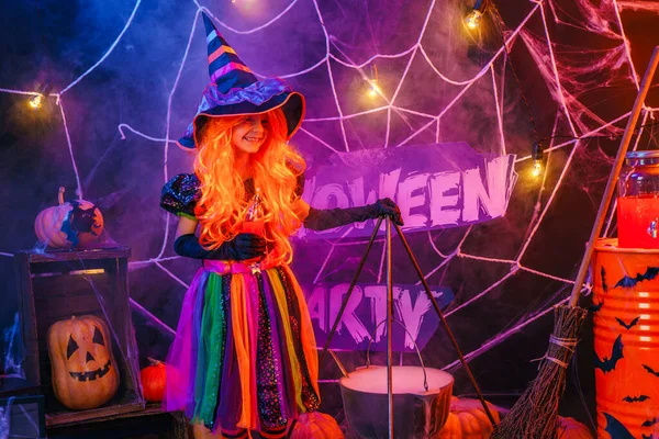 Маленькая красивая девочка в костюме ведьмы празднует Хэллоуин в интерьере с тыквами — стоковое фото